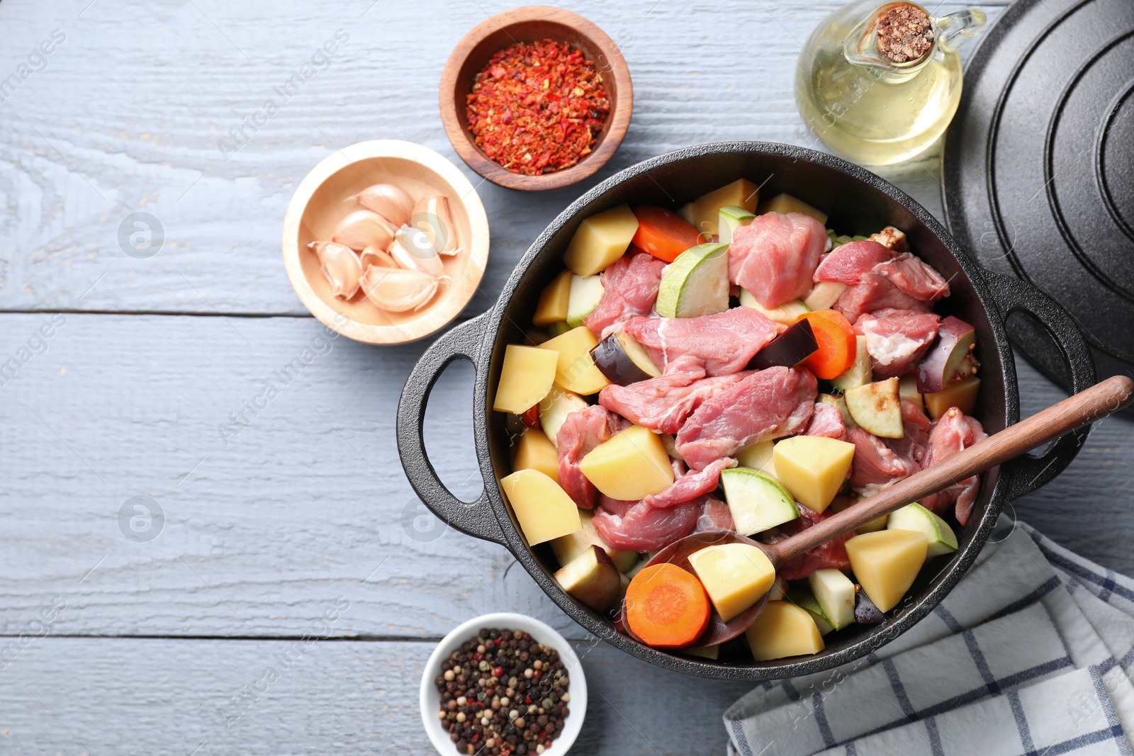 Photo of Cooking stew. Uncooked meat and vegetables in pot on light grey wooden table, flat lay. Space for text