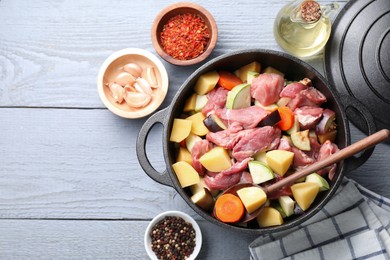 Photo of Cooking stew. Uncooked meat and vegetables in pot on light grey wooden table, flat lay. Space for text