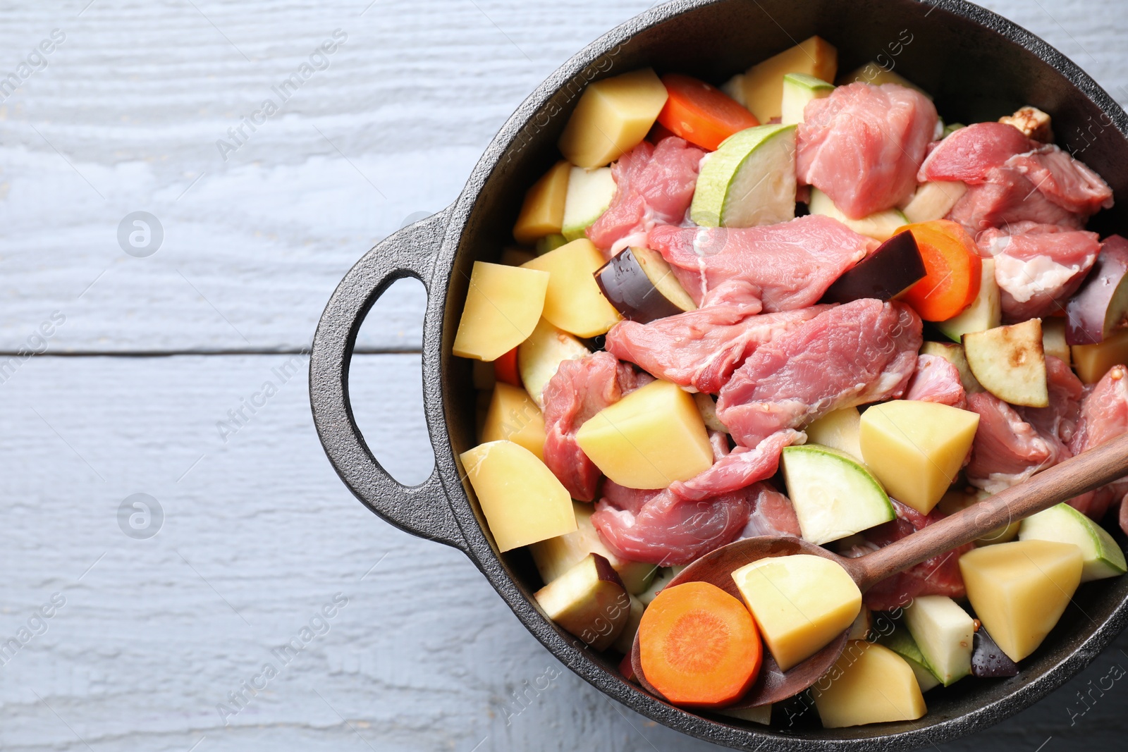 Photo of Cooking stew. Uncooked meat and vegetables in pot on light grey table, top view. Space for text