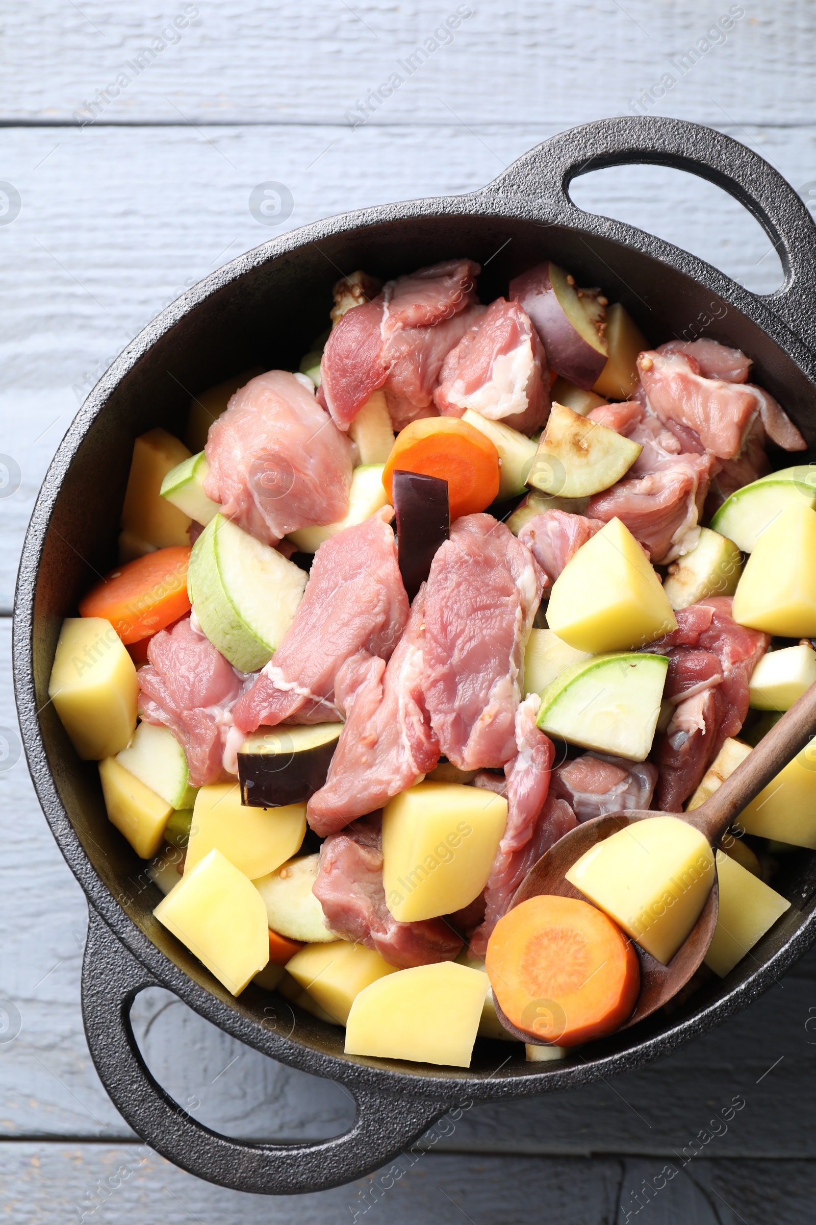 Photo of Cooking stew. Uncooked meat and vegetables in pot on light grey table, top view