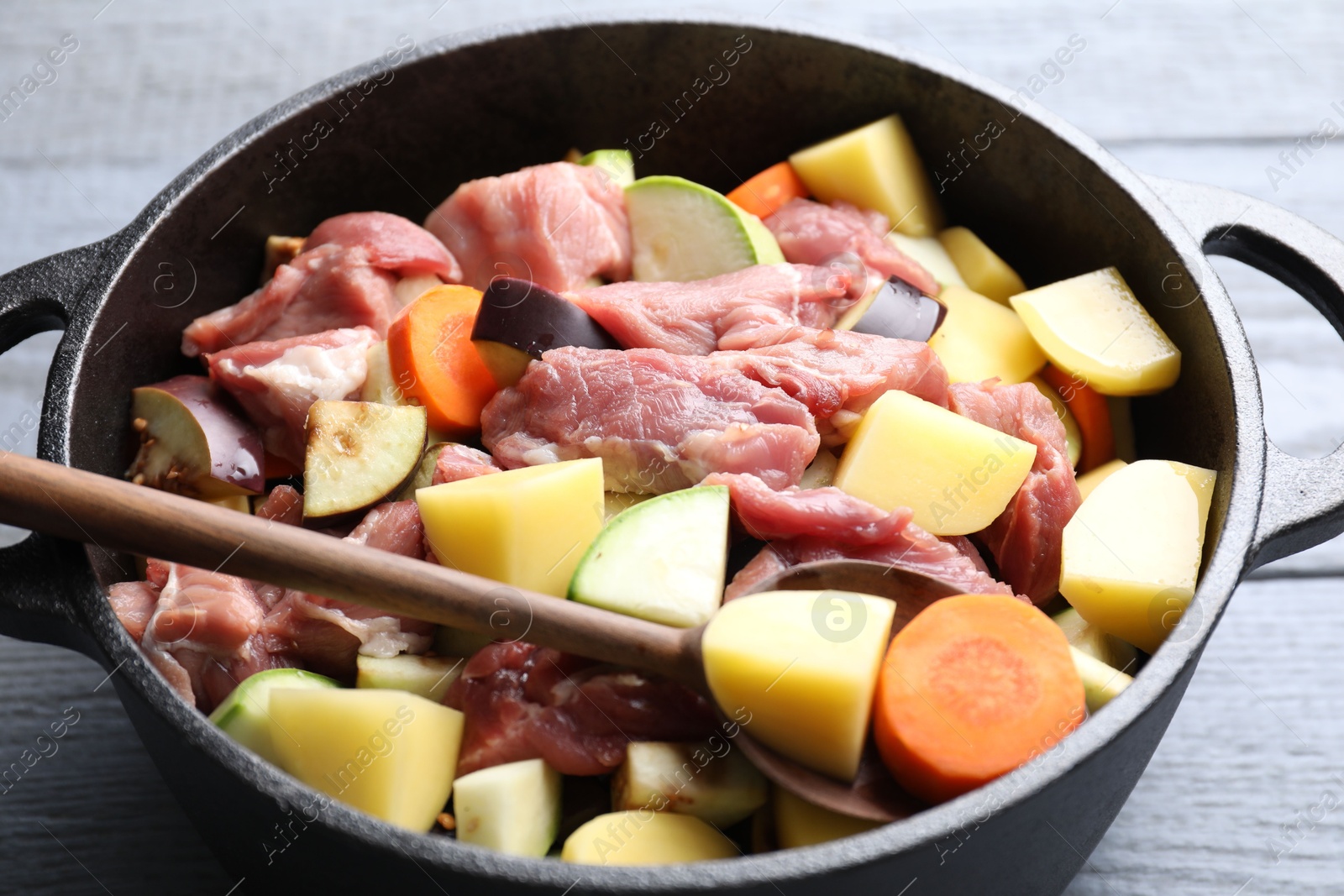 Photo of Cooking stew. Uncooked meat and vegetables in pot on light grey wooden table, closeup