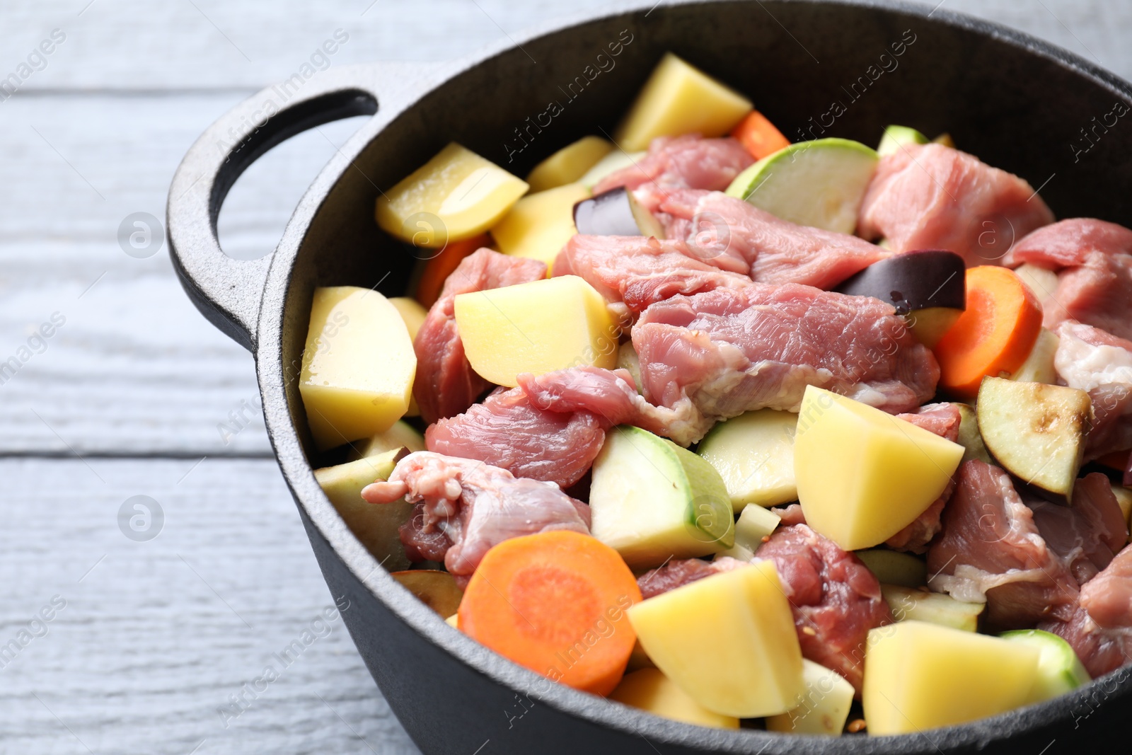 Photo of Cooking stew. Uncooked meat and vegetables in pot on light grey wooden table, closeup