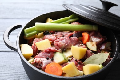 Photo of Cooking stew. Uncooked meat and vegetables in pot on light grey wooden table, closeup