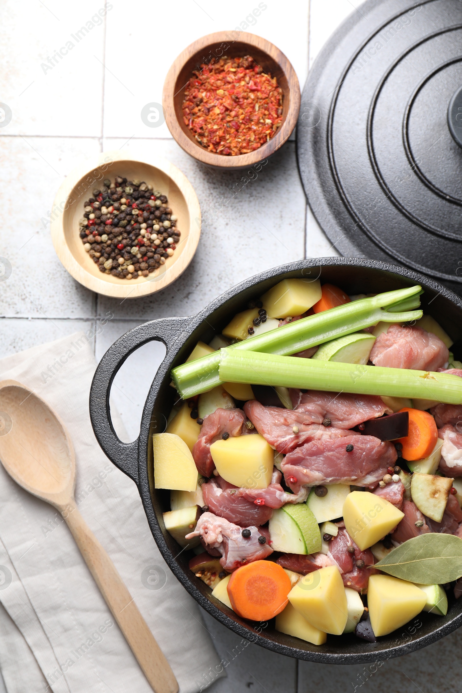 Photo of Cooking stew. Uncooked meat and vegetables in pot on white tiled table, flat lay