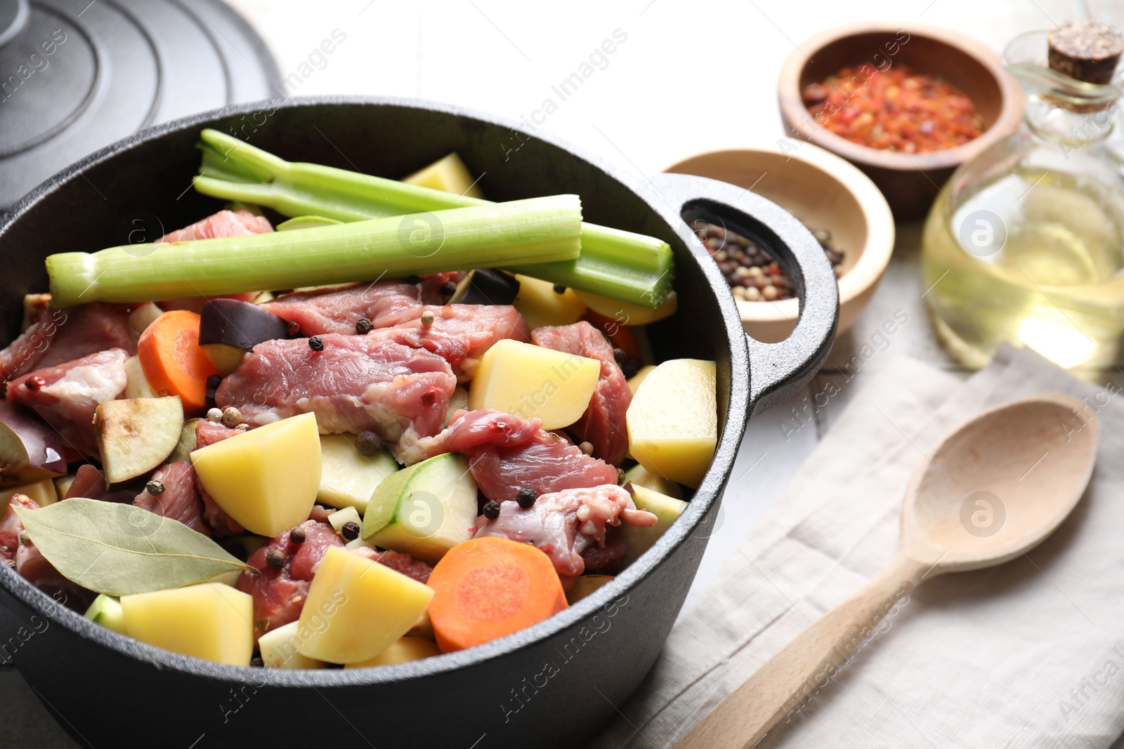 Photo of Cooking stew. Uncooked meat and vegetables in pot on white tiled table, closeup