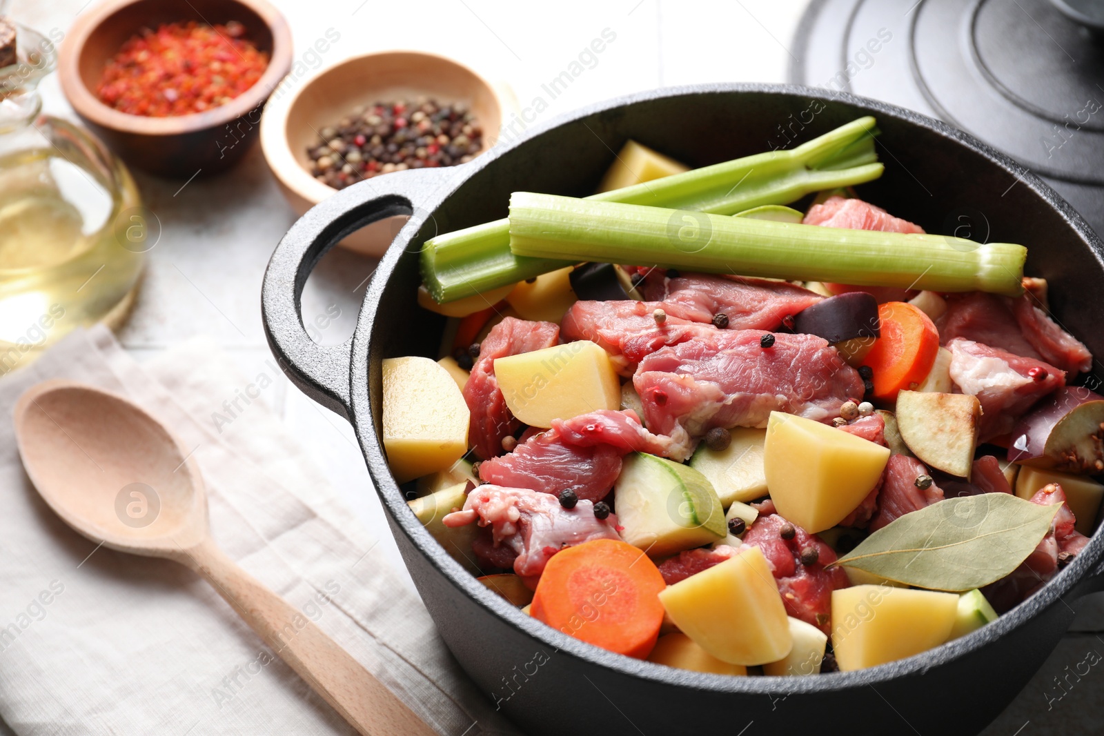 Photo of Cooking stew. Uncooked meat and vegetables in pot on white tiled table, closeup