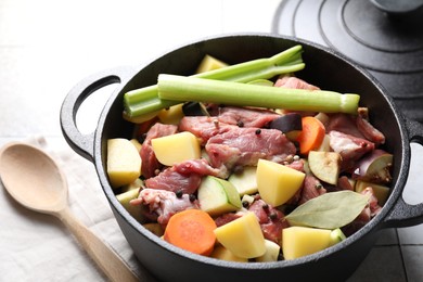 Photo of Cooking stew. Uncooked meat and vegetables in pot on white tiled table, closeup