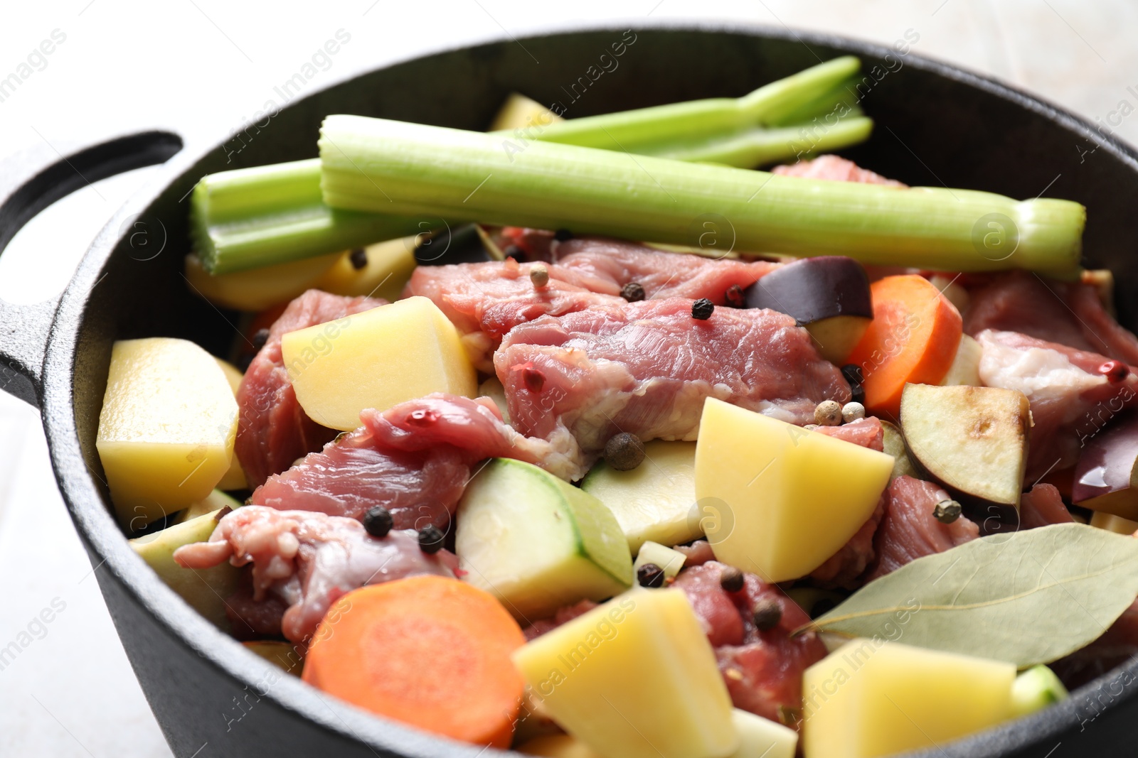 Photo of Cooking stew. Uncooked meat and vegetables in pot on white tiled table, closeup