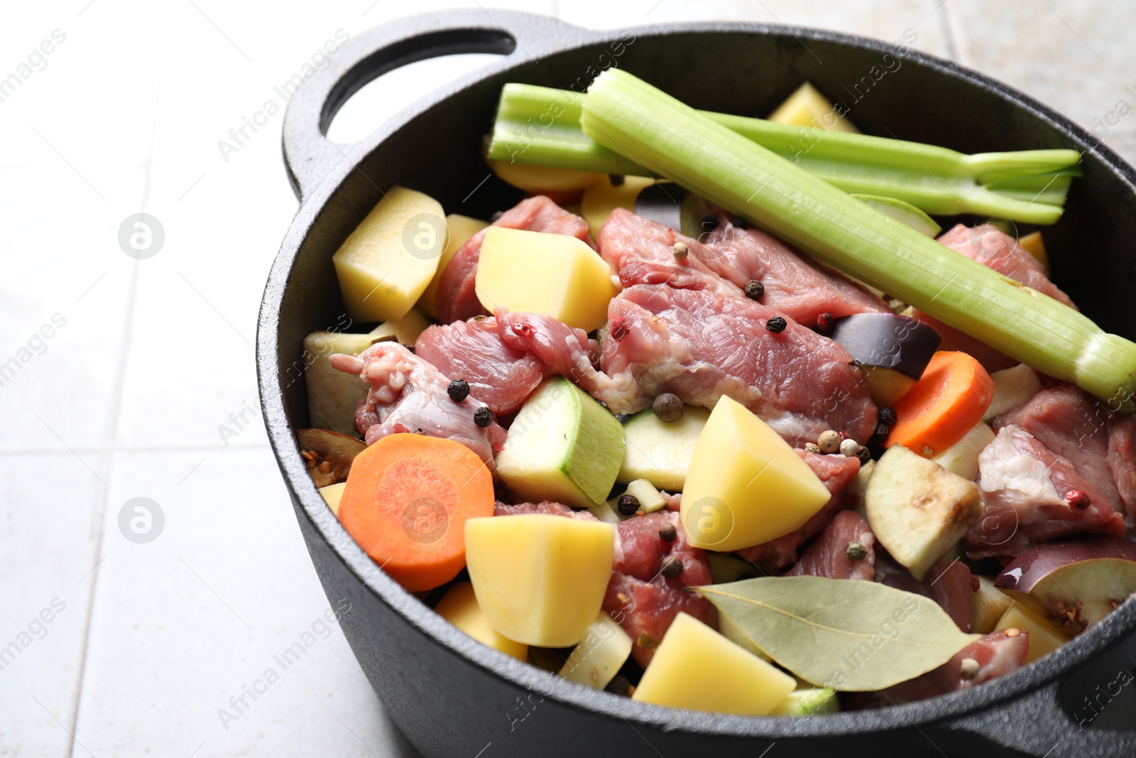 Photo of Cooking stew. Uncooked meat and vegetables in pot on white tiled table, closeup