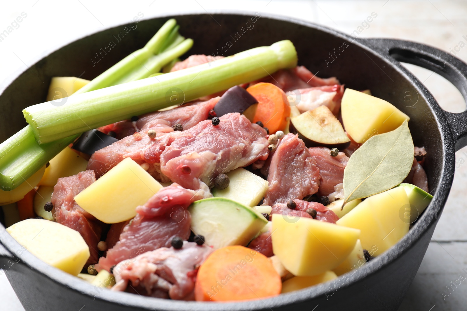 Photo of Cooking stew. Uncooked meat and vegetables in pot on white tiled table, closeup