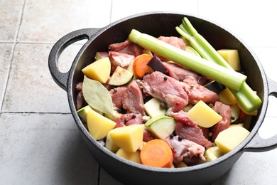 Photo of Cooking stew. Uncooked meat and vegetables in pot on white tiled table