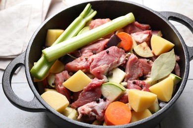 Photo of Cooking stew. Uncooked meat and vegetables in pot on white tiled table, closeup