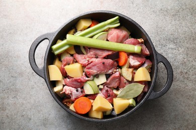 Photo of Cooking stew. Uncooked meat and vegetables in pot on light grey table, top view