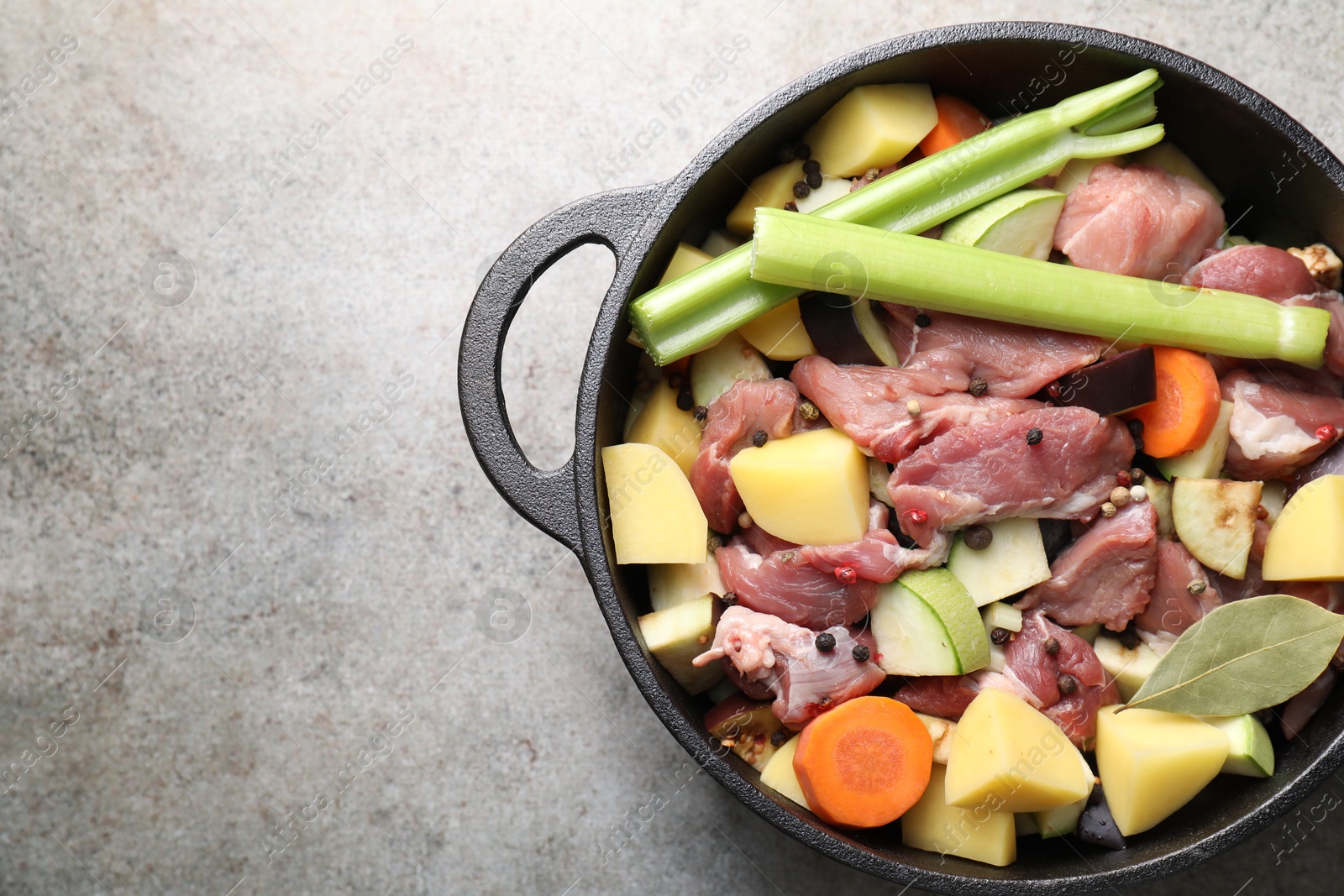 Photo of Cooking stew. Uncooked meat and vegetables in pot on light grey table, top view. Space for text