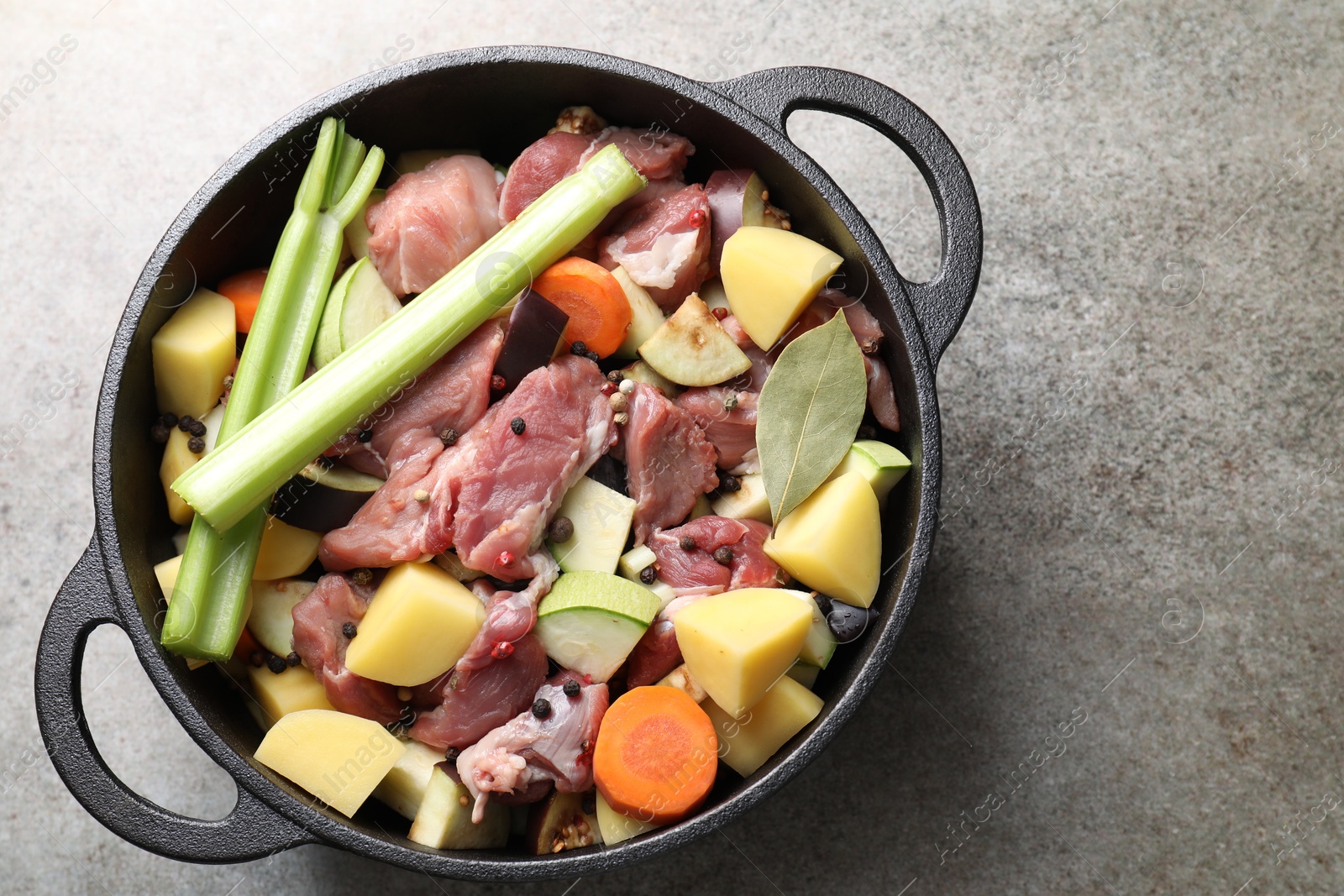 Photo of Cooking stew. Uncooked meat and vegetables in pot on light grey table, top view