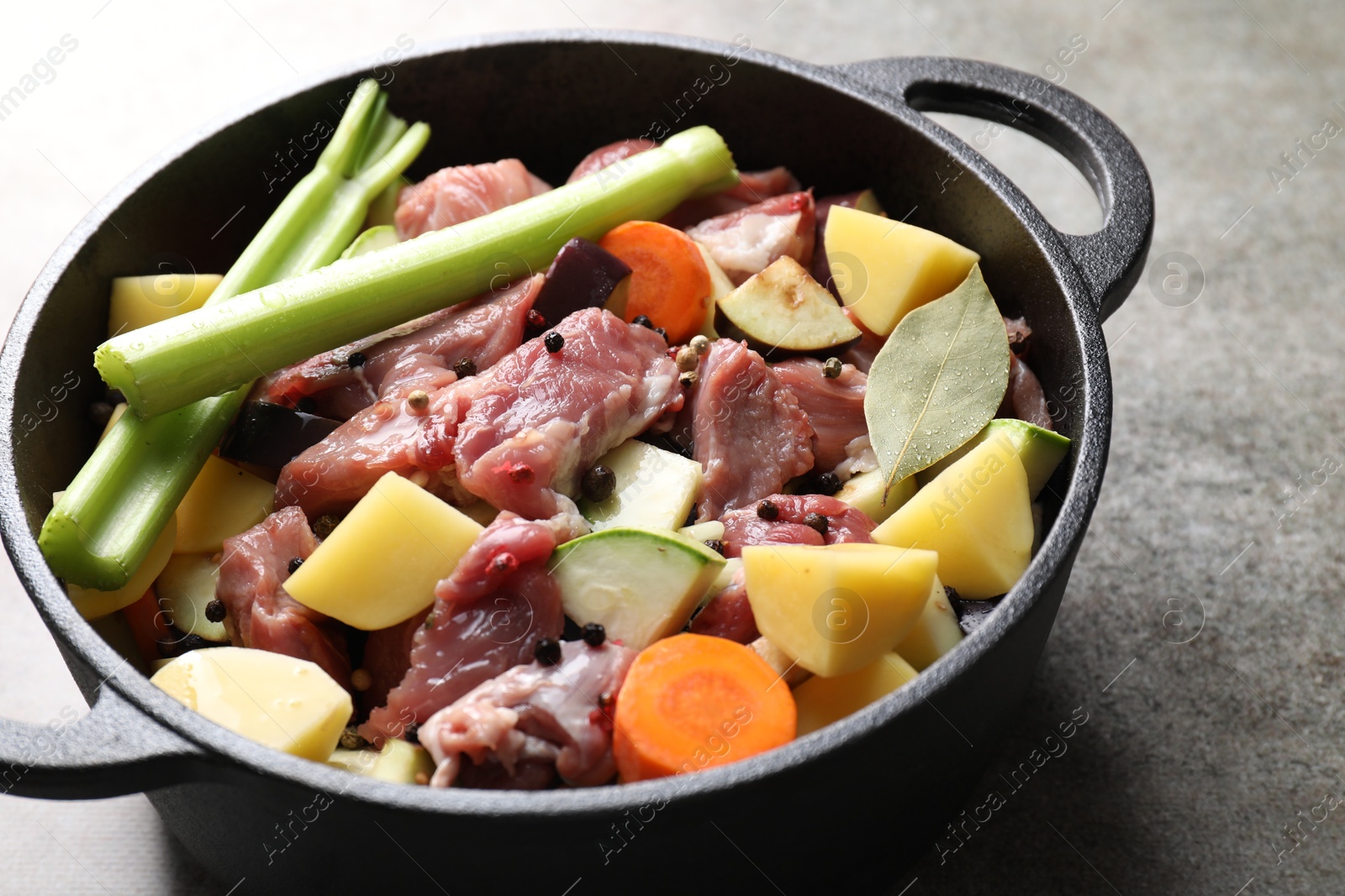 Photo of Cooking stew. Uncooked meat and vegetables in pot on light grey table, closeup