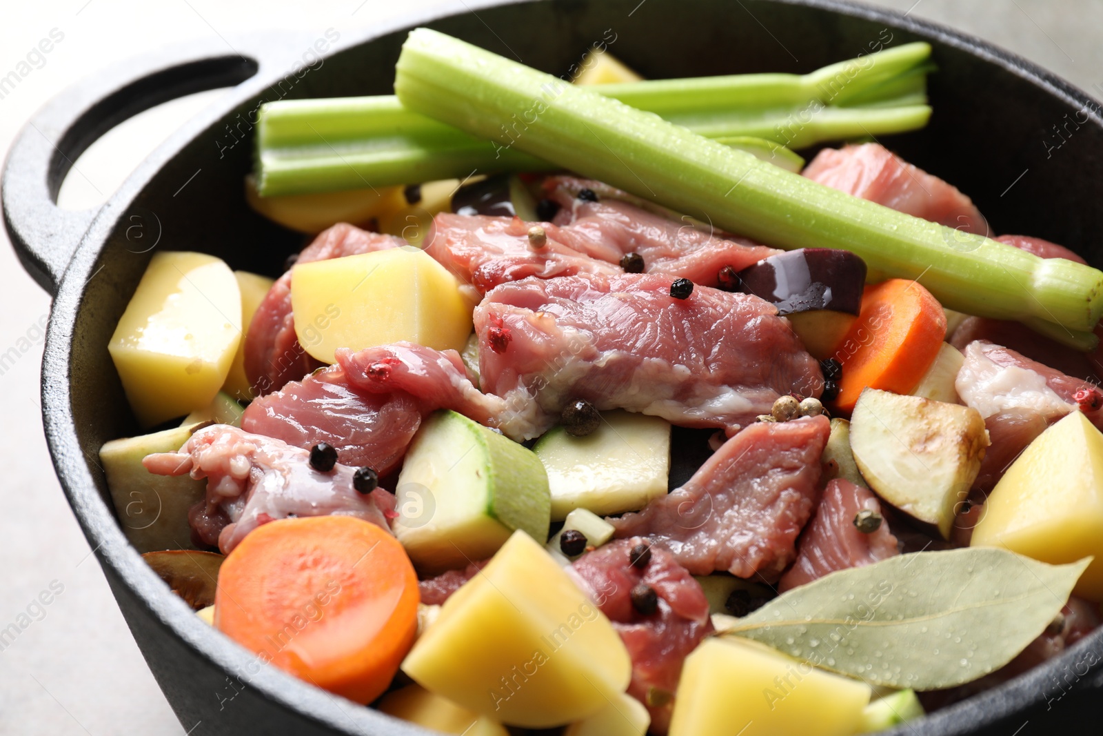 Photo of Cooking stew. Uncooked meat and vegetables in pot on light grey table, closeup