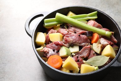 Photo of Cooking stew. Uncooked meat and vegetables in pot on light grey table, closeup