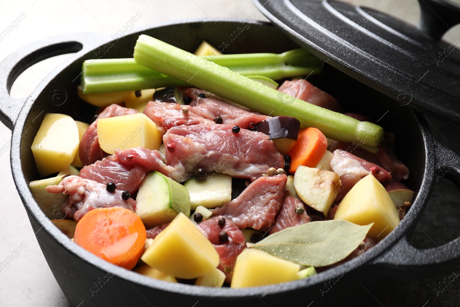 Photo of Cooking stew. Uncooked meat and vegetables in pot on light grey table, closeup