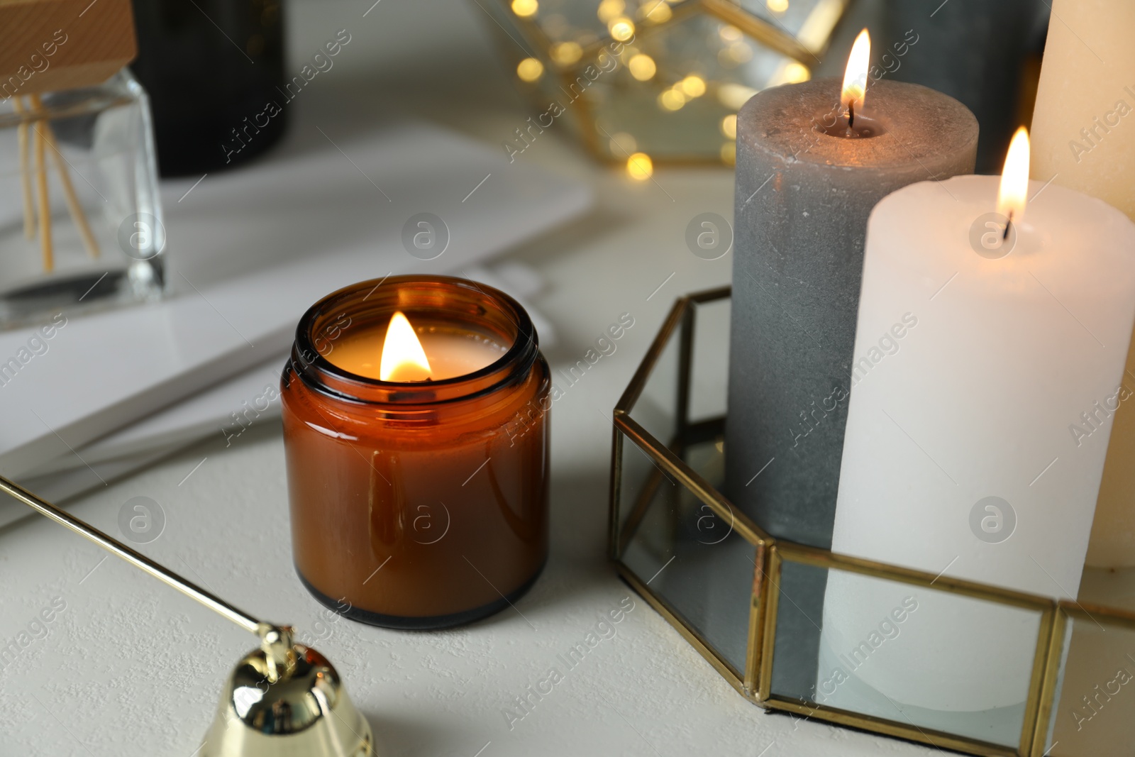 Photo of Beautiful burning candles on light table against blurred lights, closeup