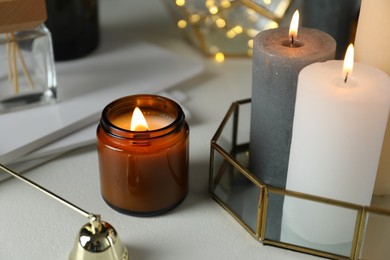 Photo of Beautiful burning candles on light table against blurred lights, closeup