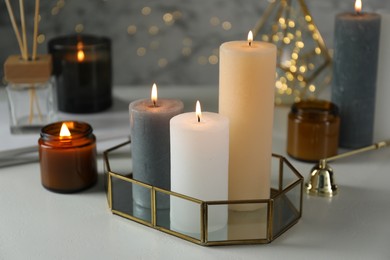 Photo of Beautiful burning candles on light table against blurred lights, closeup