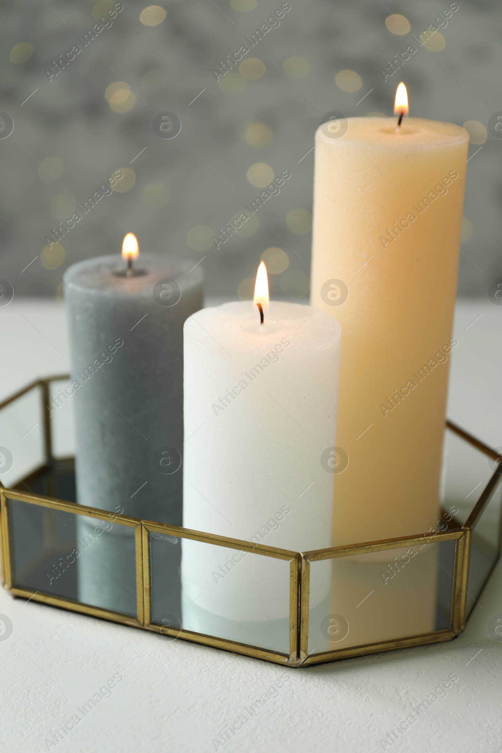 Photo of Beautiful burning candles on white table against blurred lights, closeup