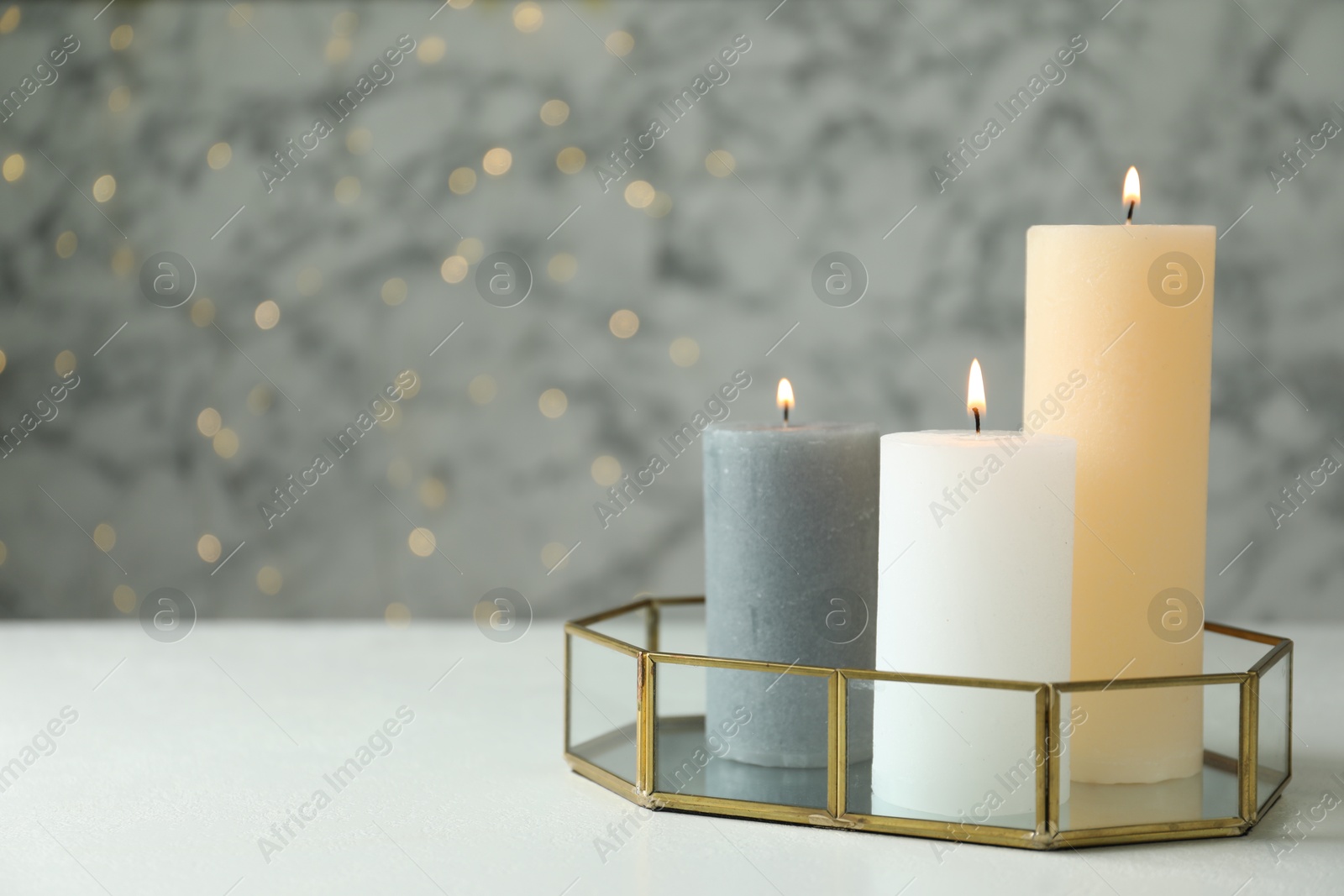 Photo of Beautiful burning candles on white table against blurred lights, space for text