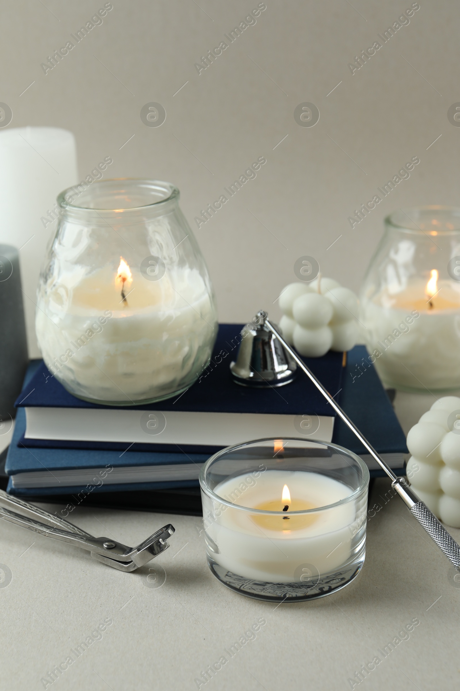 Photo of Beautiful burning candles, books, candle snuffer and wick trimmer on light background, closeup