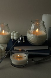 Beautiful burning candles, books, candle snuffer and wick trimmer on gray background, closeup