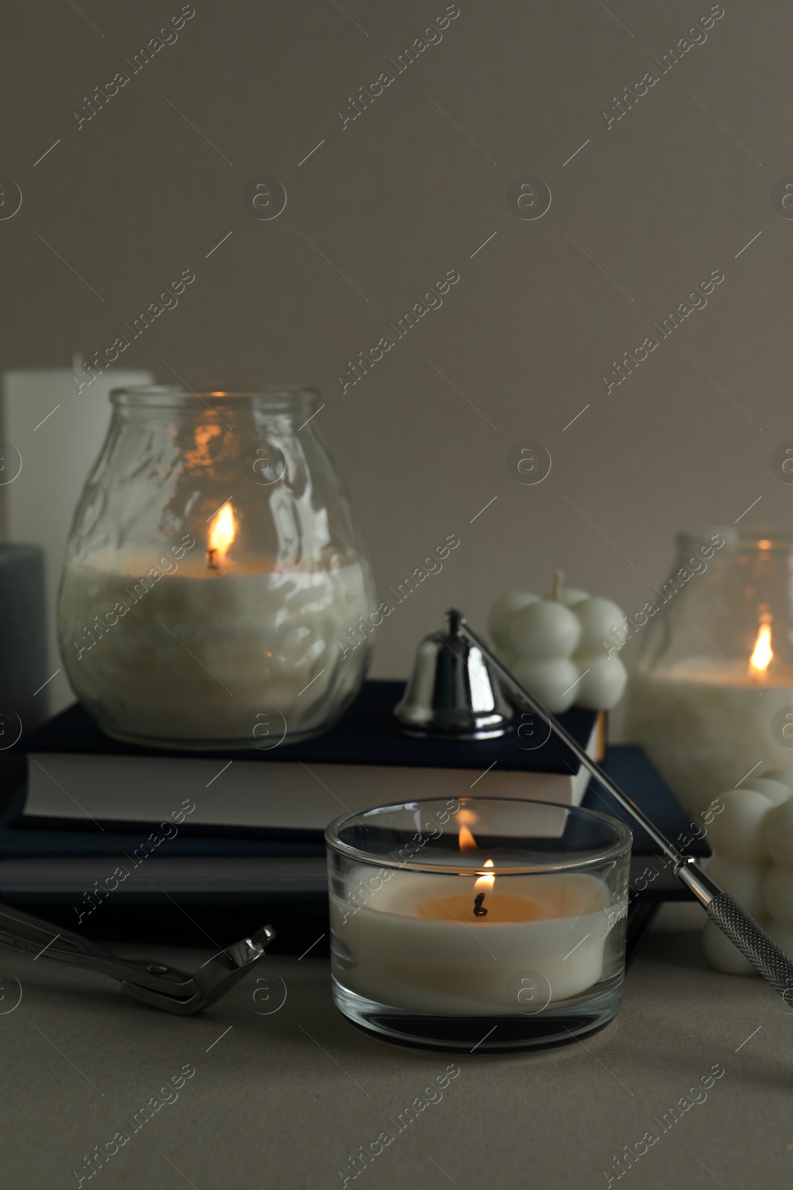 Photo of Beautiful burning candles, books, candle snuffer and wick trimmer on gray background, closeup