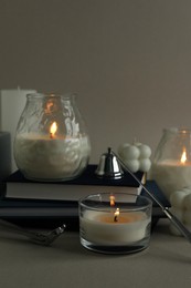 Beautiful burning candles, books, candle snuffer and wick trimmer on gray background, closeup