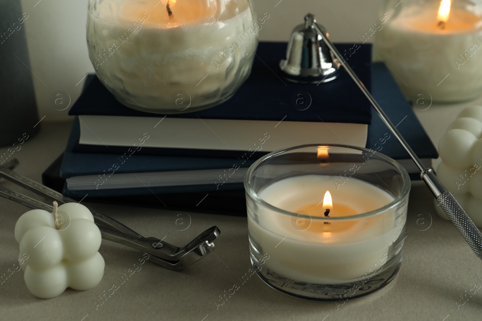 Photo of Beautiful burning candles, books, candle snuffer and wick trimmer on gray table, closeup