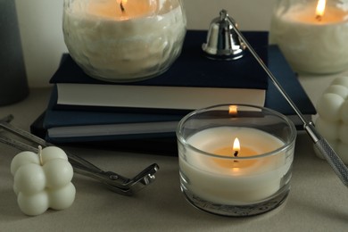 Beautiful burning candles, books, candle snuffer and wick trimmer on gray table, closeup