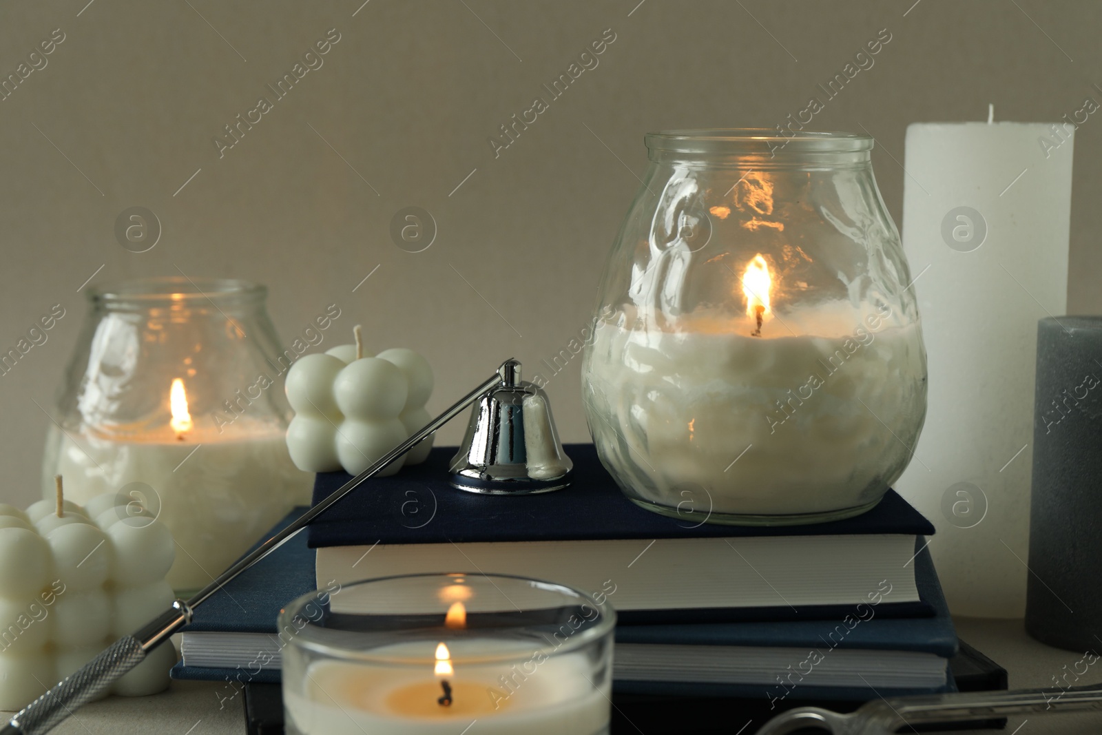 Photo of Beautiful burning candles, books, candle snuffer and wick trimmer on gray table, closeup