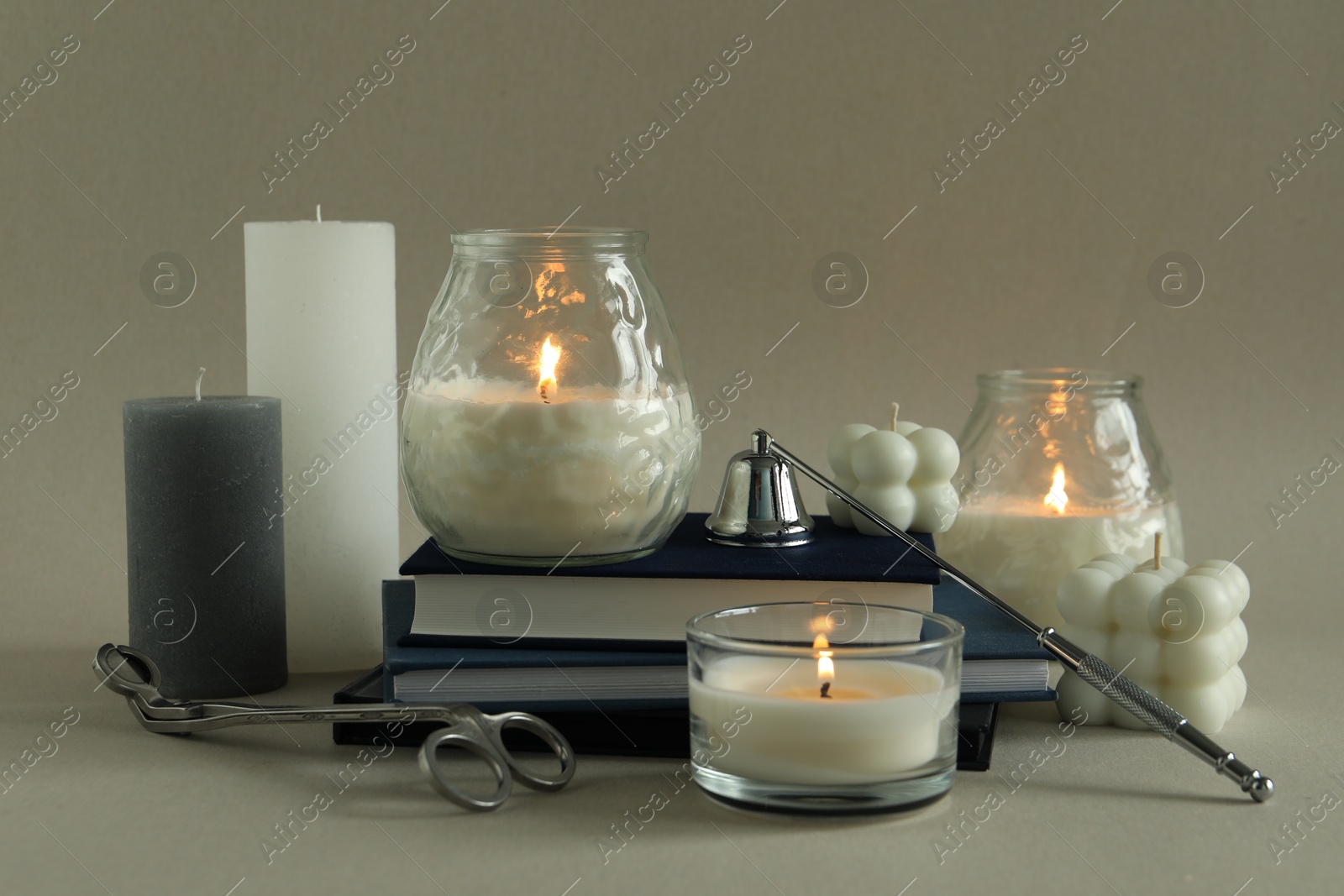 Photo of Beautiful burning candles, books, candle snuffer and wick trimmer on gray background