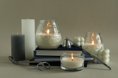 Beautiful burning candles, books, candle snuffer and wick trimmer on gray background