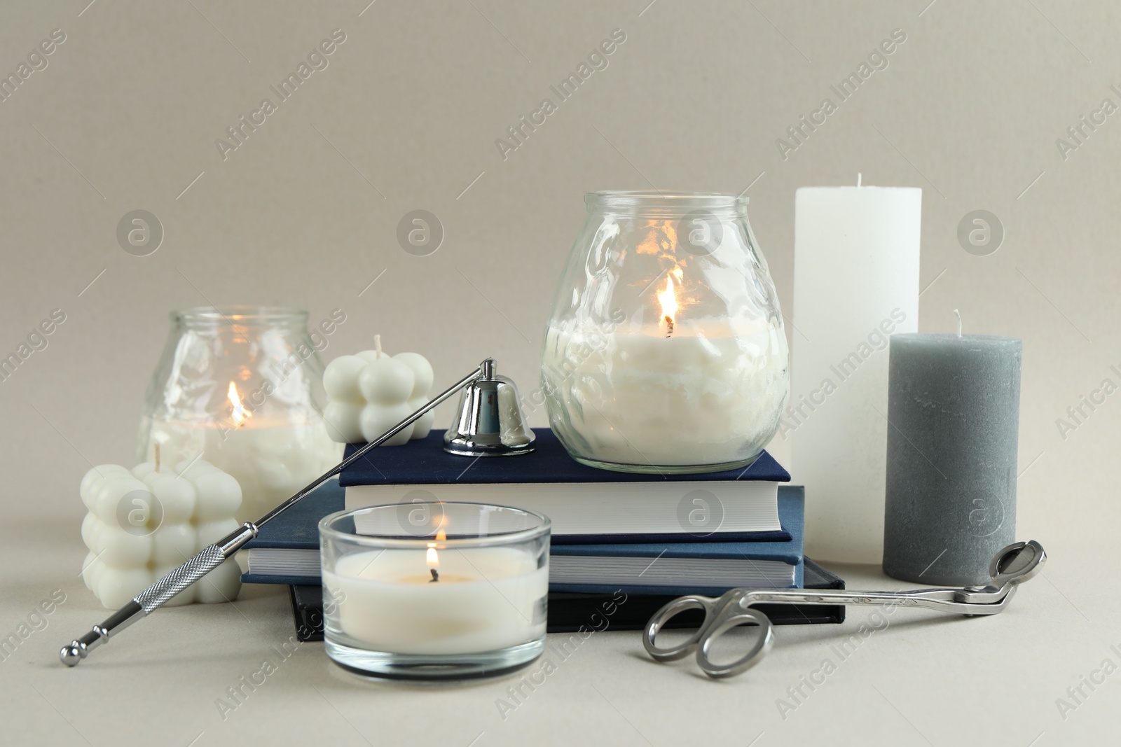 Photo of Beautiful burning candles, books, candle snuffer and wick trimmer on light background