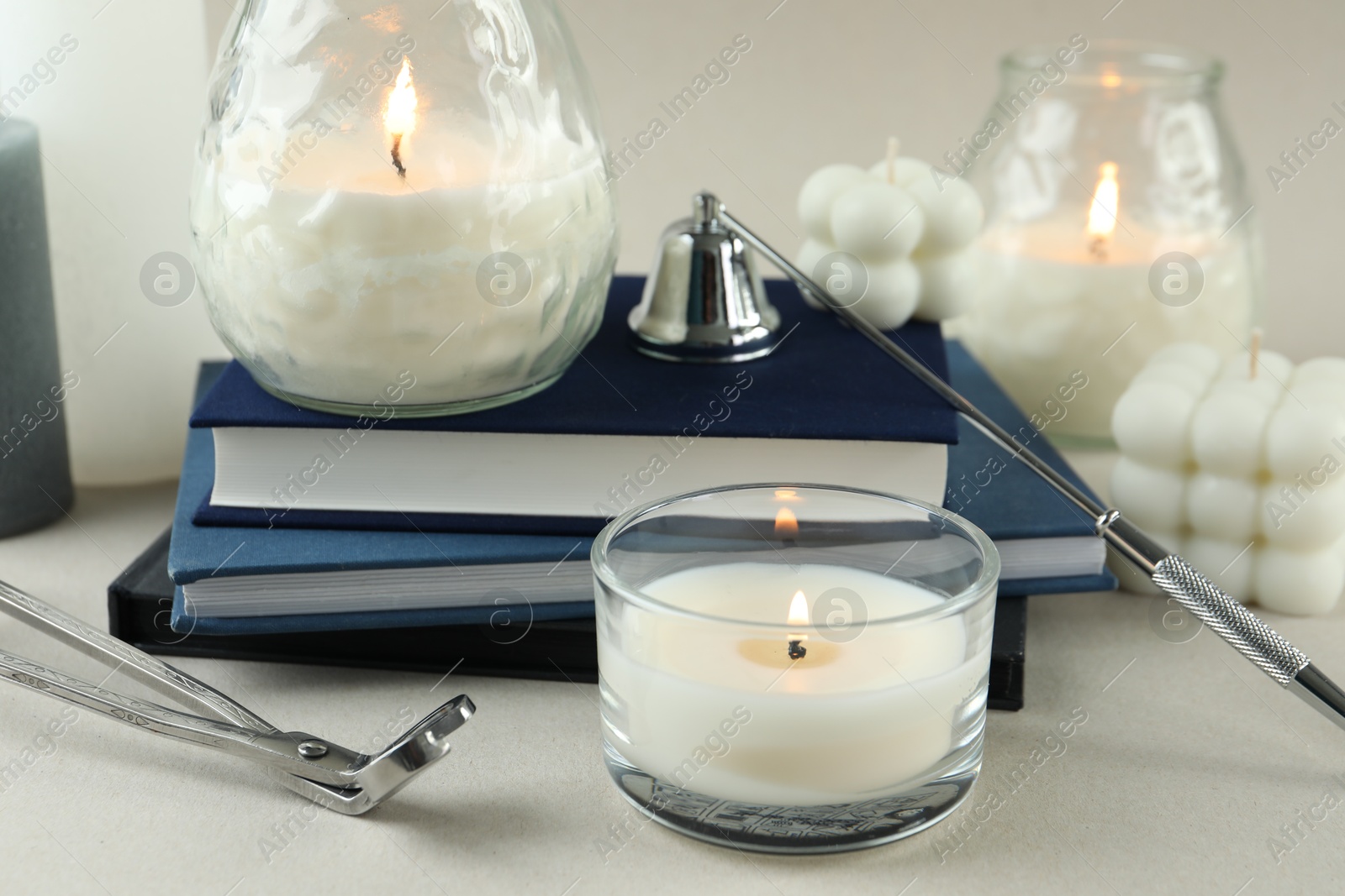 Photo of Beautiful burning candles, books, candle snuffer and wick trimmer on light table, closeup