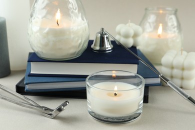 Beautiful burning candles, books, candle snuffer and wick trimmer on light table, closeup