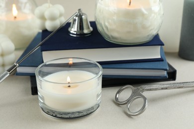 Beautiful burning candles, books, candle snuffer and wick trimmer on light table, closeup