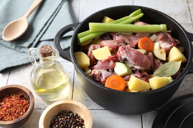 Photo of Cooking stew. Uncooked meat and vegetables in pot on white tiled table