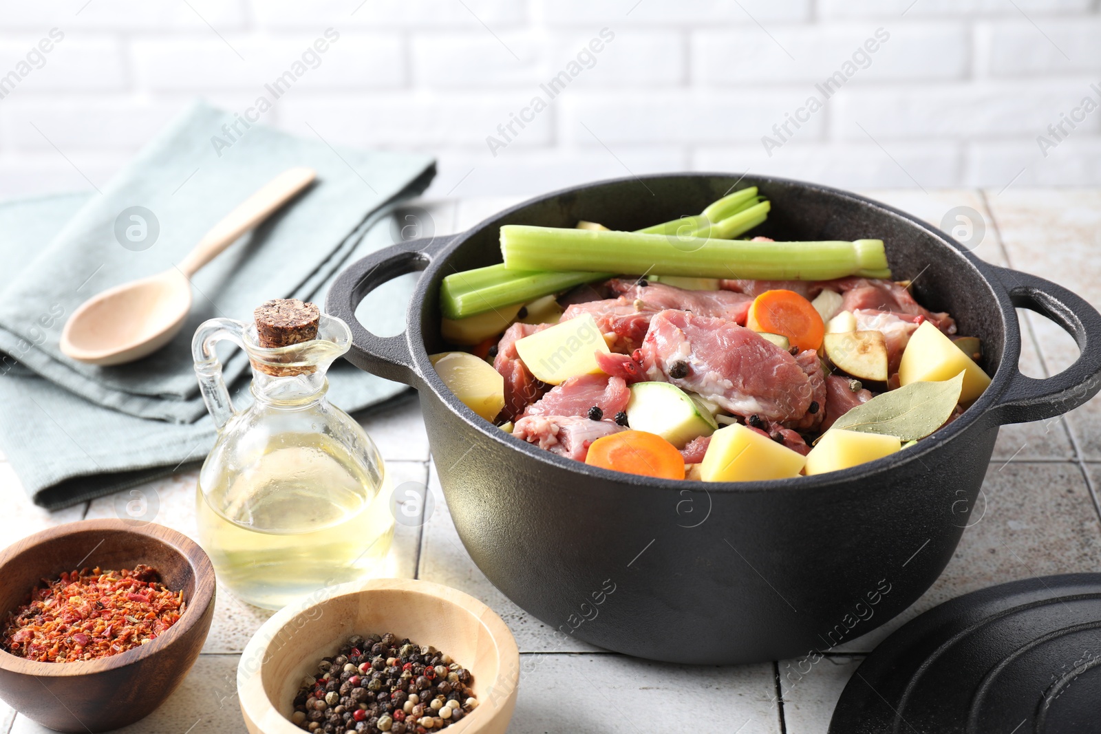 Photo of Cooking stew. Uncooked meat and vegetables in pot on white tiled table