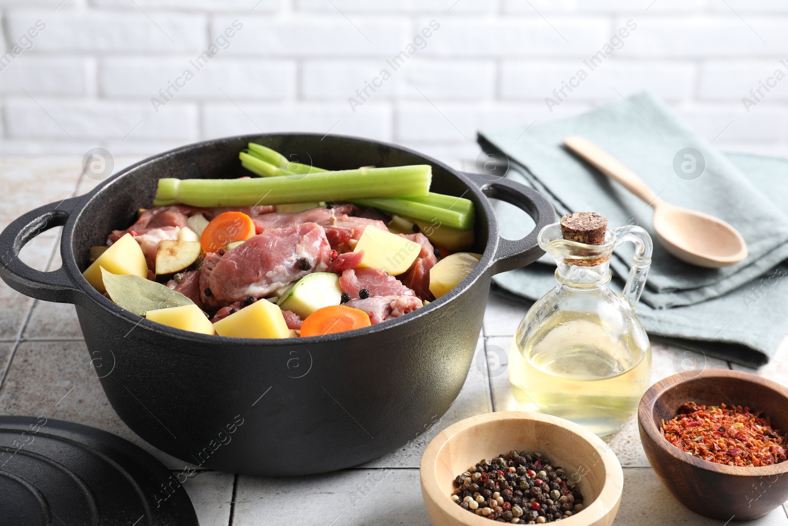 Photo of Cooking stew. Uncooked meat and vegetables in pot on white tiled table