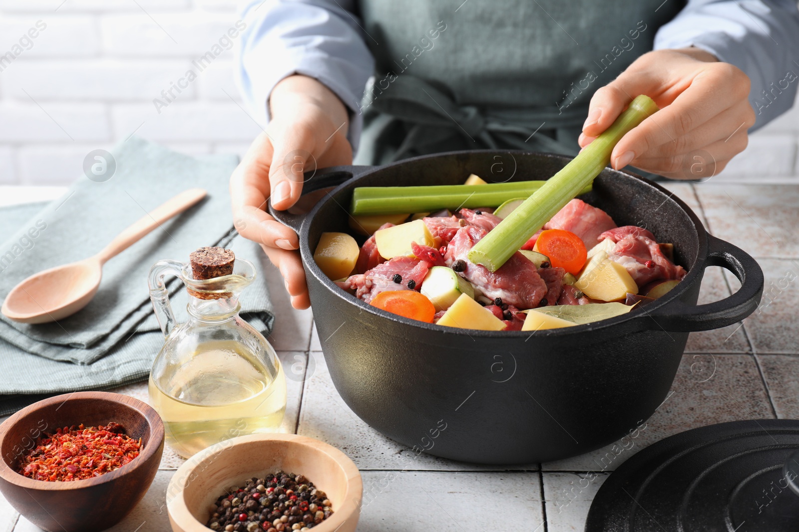 Photo of Woman preparing stew with vegetables and meat at white tiled table, closeup