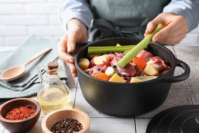 Photo of Woman preparing stew with vegetables and meat at white tiled table, closeup