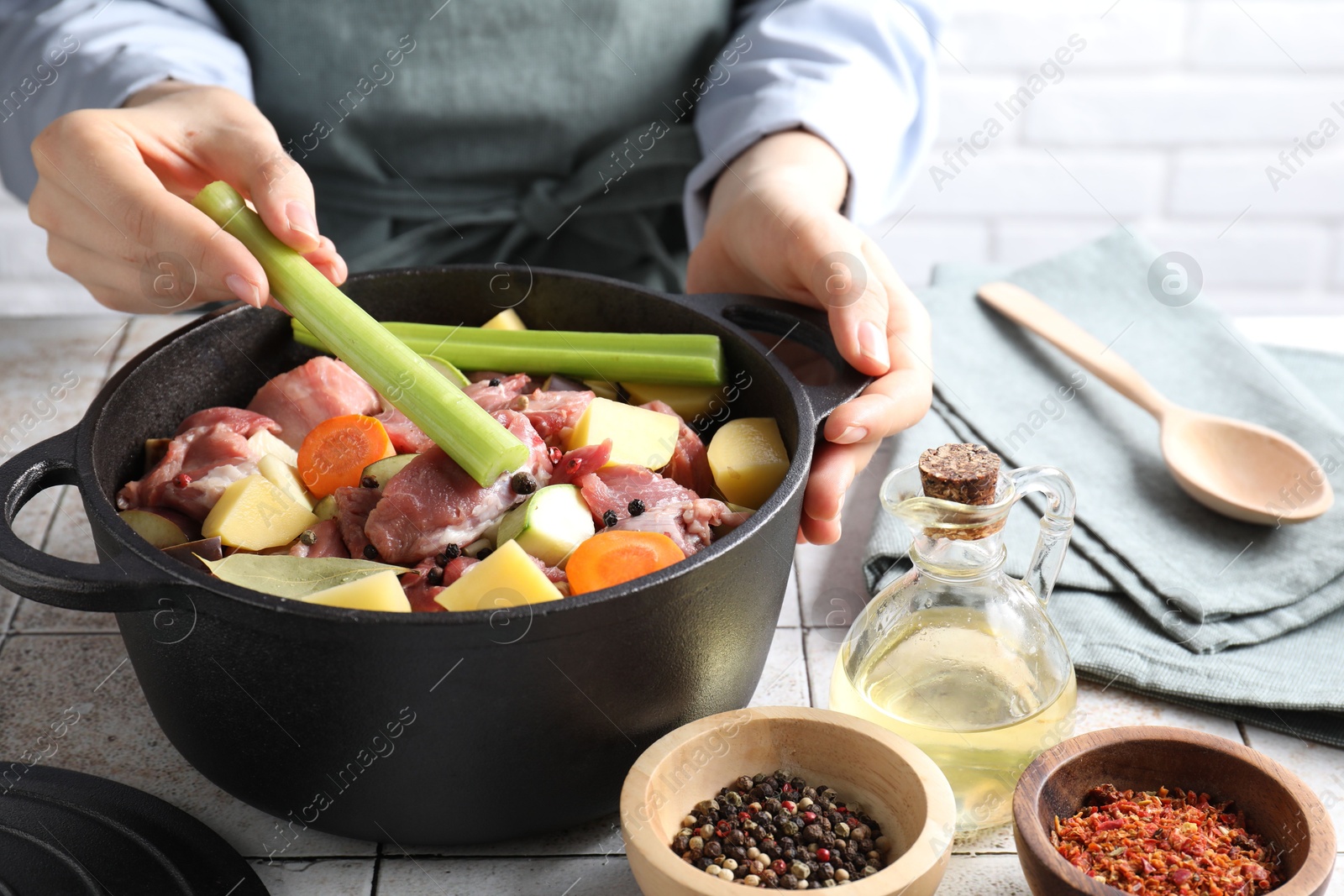 Photo of Woman preparing stew with vegetables and meat at white tiled table, closeup