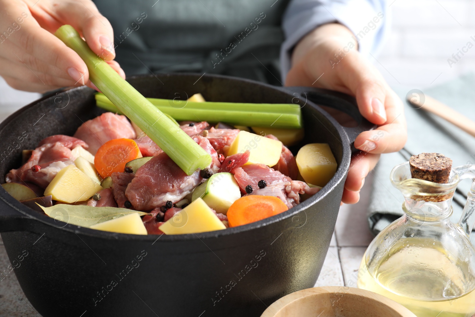 Photo of Woman preparing stew with vegetables and meat at white tiled table, closeup