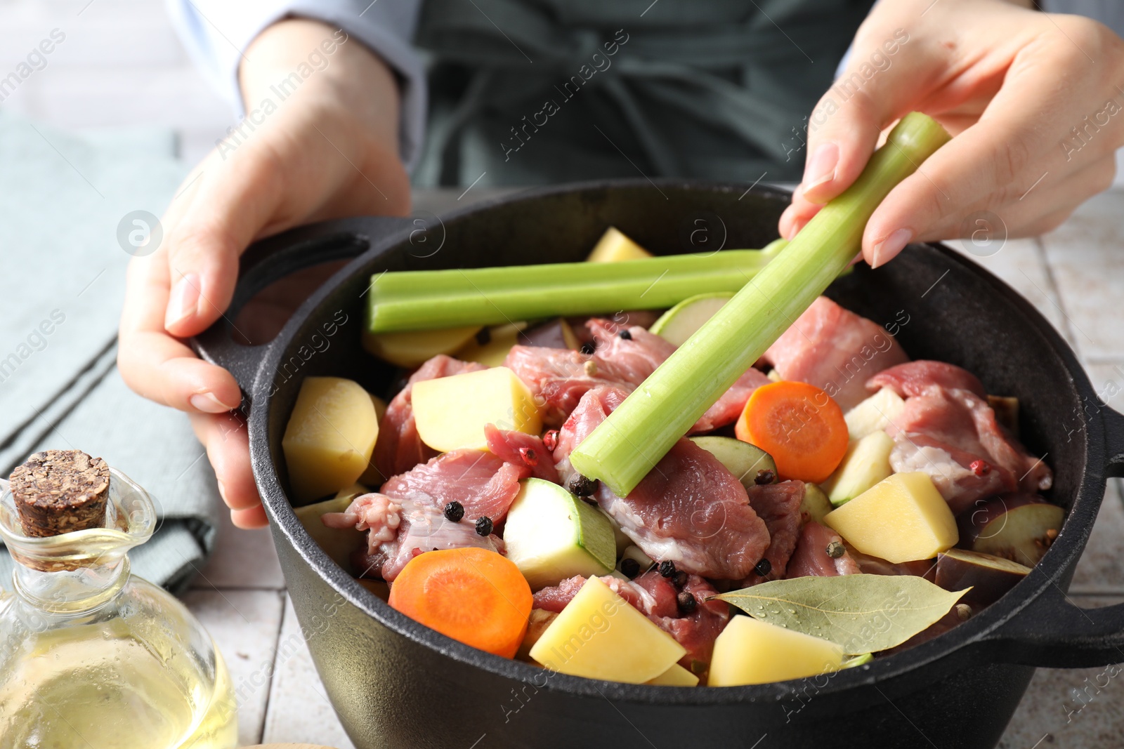 Photo of Woman preparing stew with vegetables and meat at white tiled table, closeup