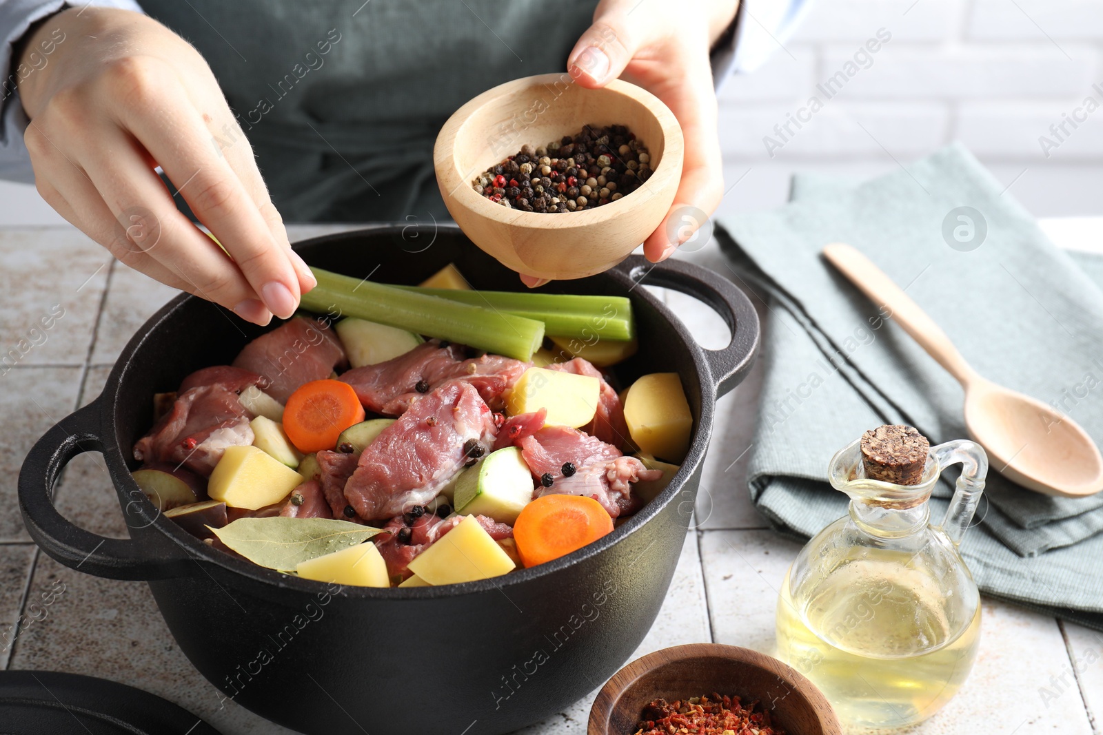 Photo of Woman preparing stew with vegetables and meat at white tiled table, closeup